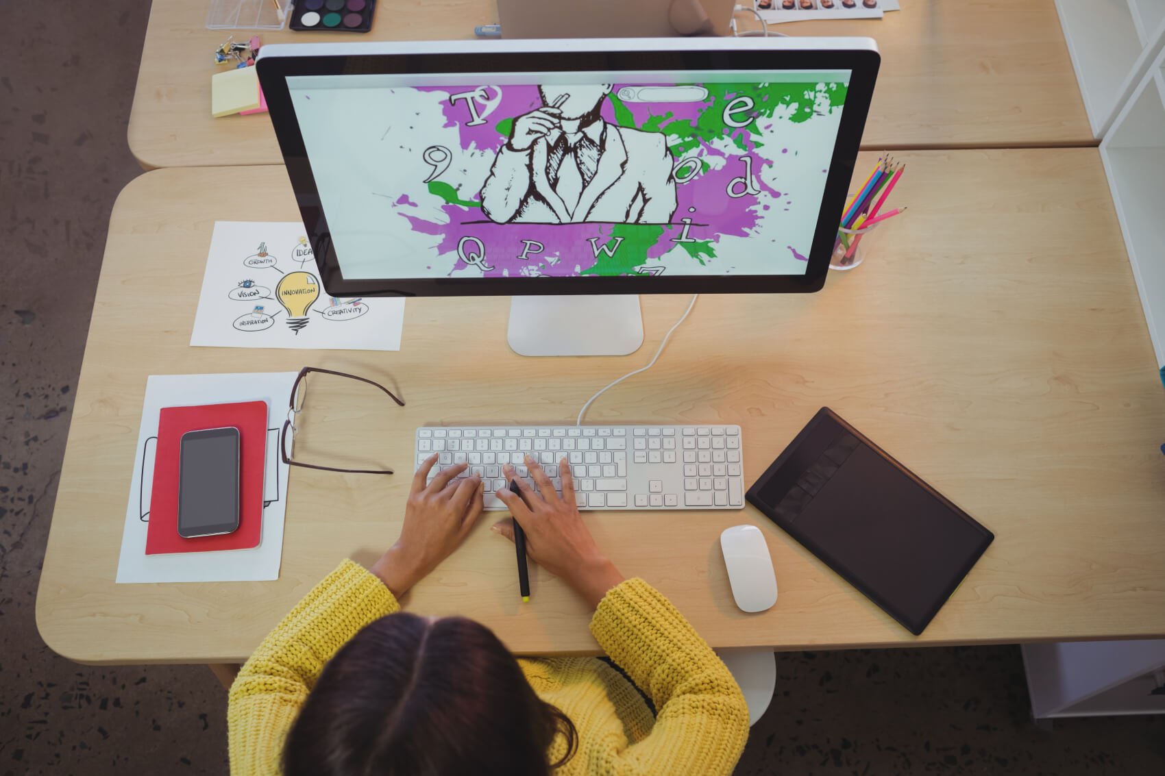 a person sitting at a desk with a computer and a screen with a drawing on it